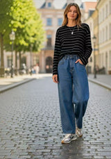 Model styling the black and white Joyjocey Relaxed Striped Long-Sleeve Top with blue jeans on a city street.
