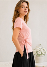 Side view of a model wearing the pink Joyjocey Side-Tie Cotton Top with its tied waist and asymmetrical hem.